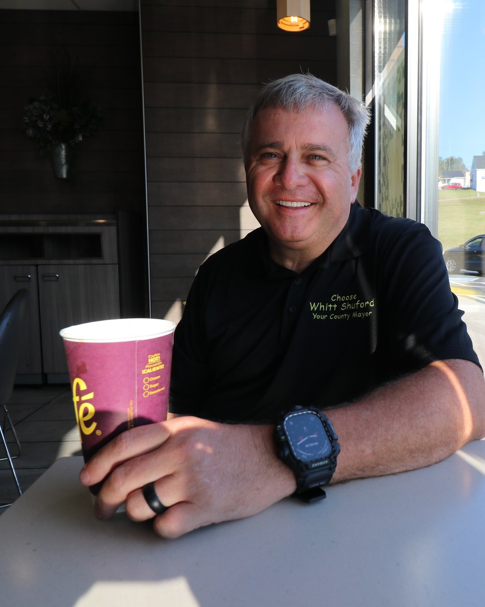 Whitt Shuford smiling at a table with a coffee cup during a Coffee with the Candidate morning
