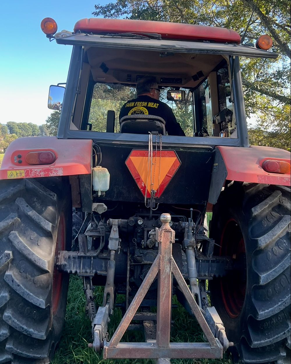 Whitt Shuford at the wheel of his tractor in a pasture, wearing the Farm Fresh Meat shirt from the farm's meat market