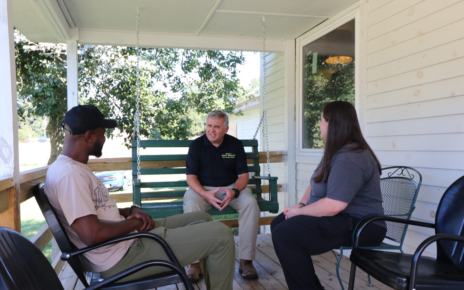 Whitt Shuford on the porch swing at Whitt's Place, talking with two neighbors seated in chairs across from him