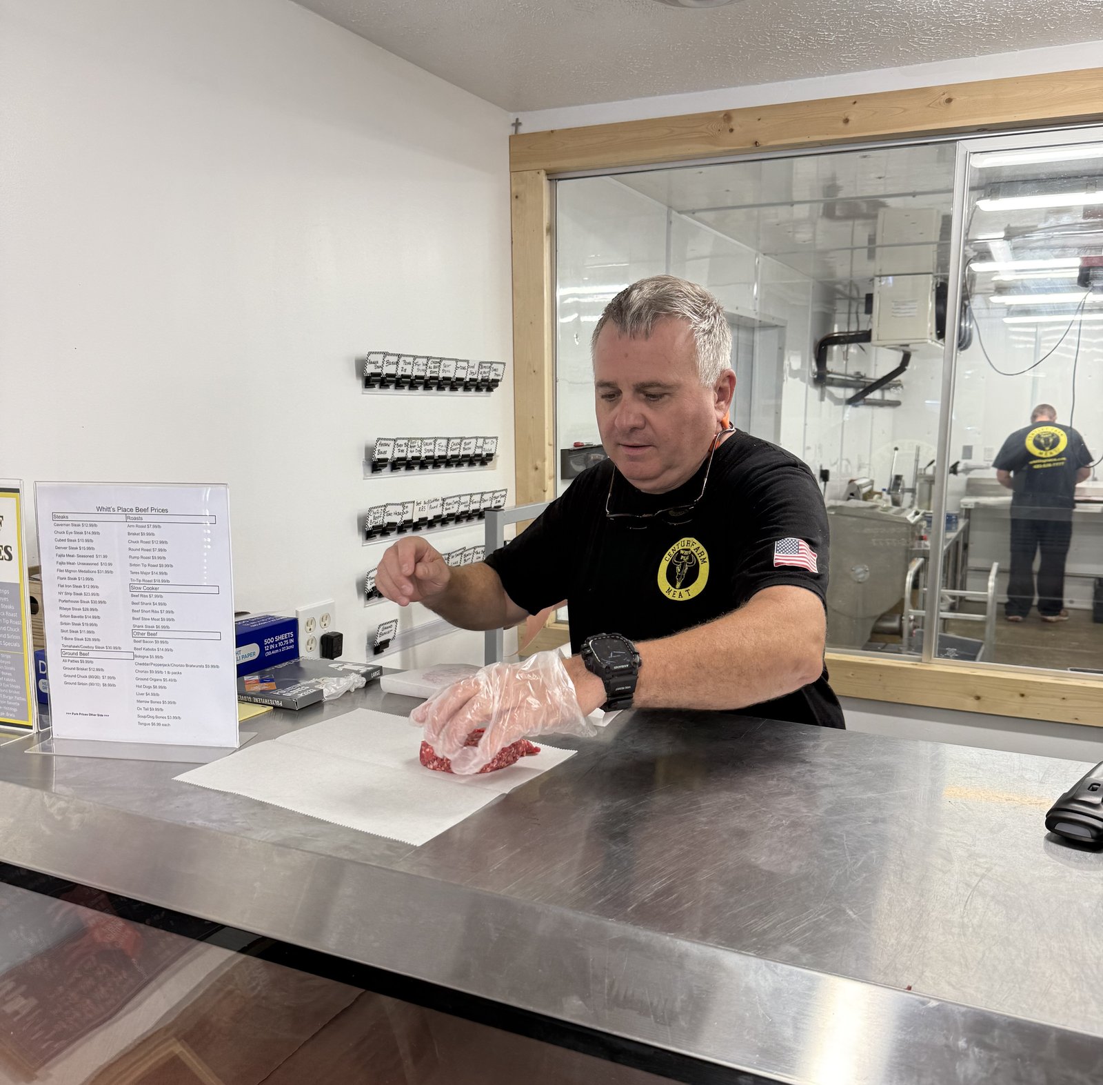 Whitt Shuford wrapping ground beef behind the counter at Whitt's Place, the Century Farm Meat logo on his shirt
